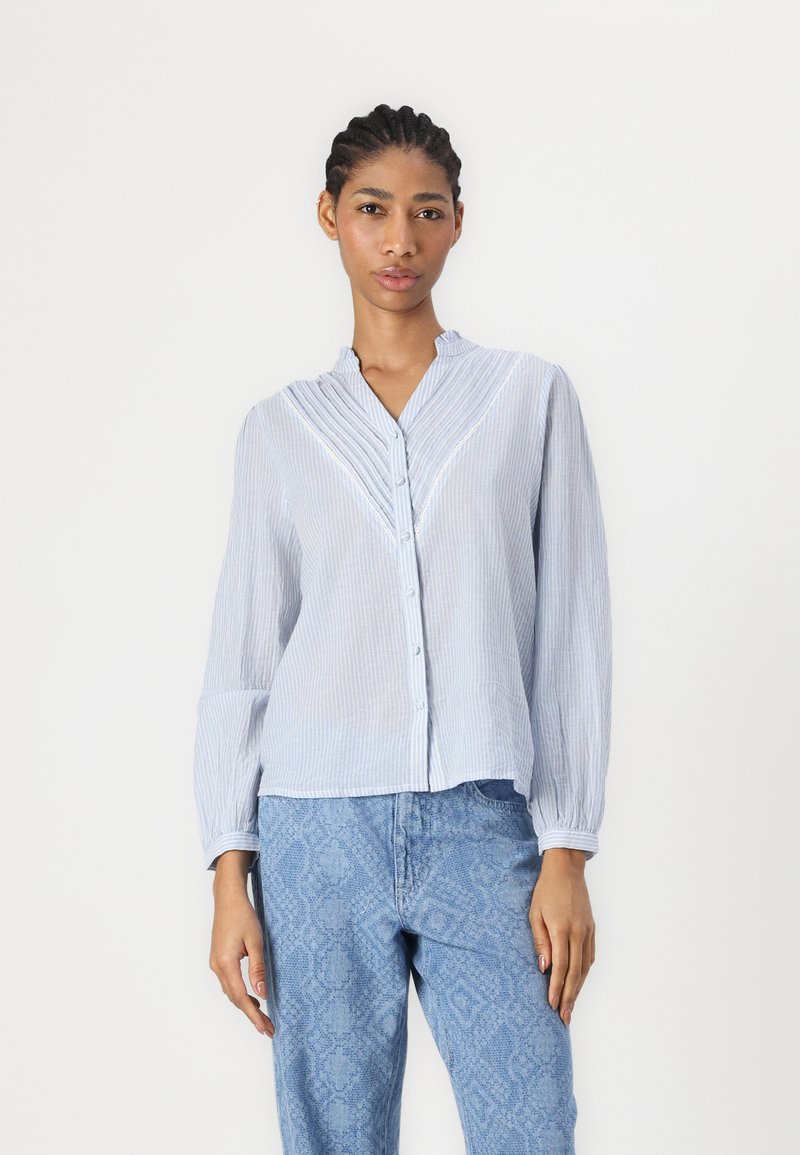 Camicia a righe blu e bianche con colletto, fronte plissettato e maniche lunghe, abbinata a pantaloni chiari in denim testurizzati.