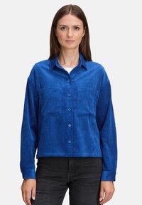 Niebieska koszula z materiału sztruksowego z guzikiem z przodu, długimi rękawami, dwiema kieszeniami z przodu i luźnym krojem, z charakterystyczną prążkowaną teksturą.
