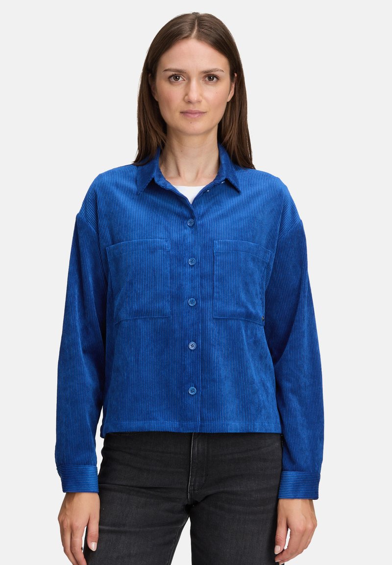 Niebieska koszula z materiału sztruksowego z guzikiem z przodu, długimi rękawami, dwiema kieszeniami z przodu i luźnym krojem, z charakterystyczną prążkowaną teksturą.