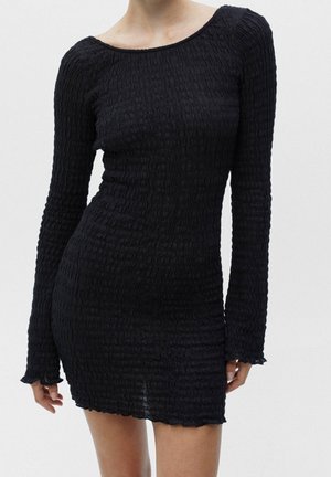 Robe noire à manches longues en tissu froissé avec un décolleté bateau. Présente une silhouette ajustée et un ourlet festonné.