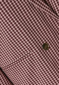 Gros plan sur un tissu à carreaux marron et blanc avec un seul bouton marron et un détail de poche cousue sur un vêtement.