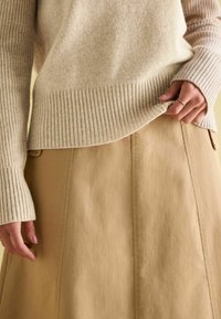 Beež ribakudum, millel on pehme tekstuur, on kokku sobitatud heleda pruunika A-line seelikuga, millel on puhtad õmblused ja sile viimistlus.