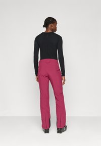 Fitted fekete hosszú ujjú felső, tapered, közepes derékú bordó nadrággal párosítva, melynek cipzáras bokái és sima textúrája van.