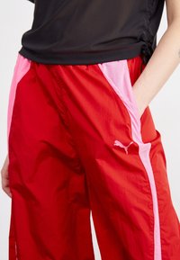 Pantalons de sport rouges avec des panneaux latéraux roses, fabriqués en matériau léger. Présentent un petit logo Puma blanc sur le devant et des poches latérales.