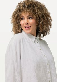 Witte, gestructureerde blouse met een kraaglijn, een voorpaneel en knoopsluiting. Lange, losse mouwen benadrukken het ontspannen ontwerp.