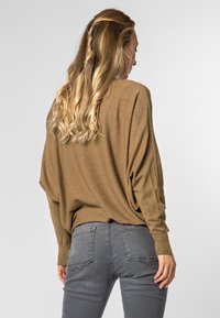 Bruine, lichte trui met een losse pasvorm en verlaagde schouders, gecombineerd met grijze, strakke jeans. Soepele textuur, geen patronen of accenten.