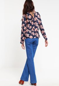 Blusa floreale con maniche lunghe, sfondo blu navy e motivo floreale rosa. Abbinata a pantaloni flare in denim blu a vita alta.