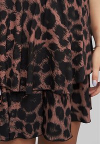 Gonna a strati con stampa leopardata marrone e nera indossata da una persona con una mano visibile e smalto bianco per unghie.