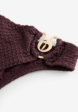 Flettet badedragtstof i mørkerød med tekstureret overflade og lås i guldtonet metal. Har elastiske samlinger i kanterne for en sikker pasform.