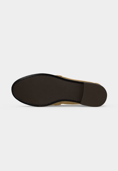 Chaussure à semelle plate avec une semelle lisse marron et une couture noire sur le bord, vue par le dessous sur un fond uni gris clair.