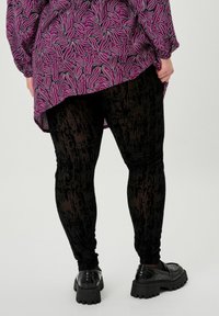 Leggings neri con texture e un motivo sottile, abbinati a un top rosa a maniche lunghe con un design astratto a contrasto. Scarpe con platform nere.