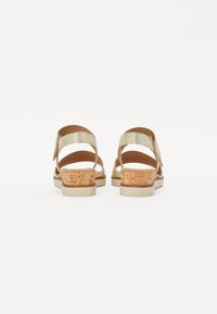 Gold heeled sandals featuring a cork block heel, adjustable straps, and a textured upper. Open back design with a flat, rubber sole.