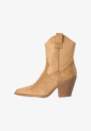 Botín cowboy de ante color beige con puntera puntiaguda, tacón de bloque apilado y lengüeta en la caña sobre fondo blanco.