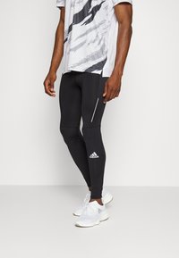 Black athletic leggings with a fitted design, featuring a white vertical stripe on the thigh and the Adidas logo in white on the lower leg.