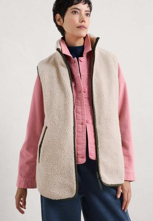 Fleece vest in crèmekleur met groene accenten, voorzien van zijzakken en een hoge kraag, gedragen over een roze overhemd met knopen. Gelaagd, warm materiaal.