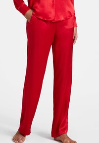 Pantalons de pyjama en satin rouge avec une coupe droite, dotés de poches latérales et d'une texture lisse et brillante. La ceinture est élastique pour plus de confort.