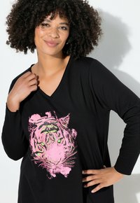 Haut à manches longues noir avec un graphique d'un visage de tigre en rose et vert. Col en V et tissu doux et texturé.