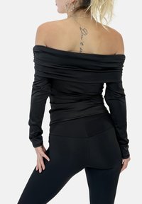 Schwarzes schulterfreies Oberteil aus weichem, dehnbarem Stoff mit langen Ärmeln und geraffter Textur, kombiniert mit schwarzen, hochtaillierten Leggings.