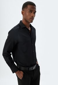 Zwarte lange mouwen button-up shirt met een kraag, textuurstof en een effen voorkant. Gecombineerd met zwarte broeken en een riem.