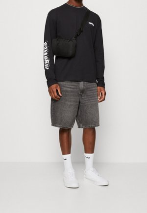 Black long-sleeve shirt with graphic print, gray denim shorts, white sneakers, and black crossbody bag. Socks are white with black logo.