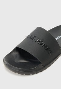 La ciabatta nera presenta una larga fascia con il logo "Jack & Jones" in rilievo, una superficie testurizzata e una suola sagomata per il massimo comfort.