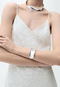 Vit blommig spetsklänning med tunna band, tillsammans med en glänsande silverhalsband och manschettarmband, med släta ytor och modern design.