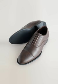 Chaussures de ville en cuir brun avec une texture lisse, bout rond, design à bout rabattu, six œillets et semelle en caoutchouc.