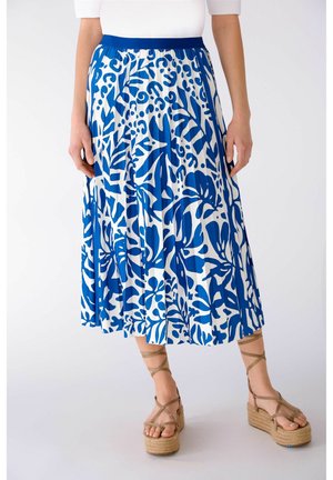 Jupe plissée bleue et blanche à motif floral abstrait. Taille élastique, portée avec des sandales compensées couleur sable.