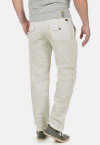 Pantalons en lin clair avec une coupe décontractée, dotés de deux poches arrière avec fermeture à bouton et d'une texture lisse.
