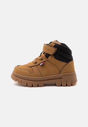 Stivale alto marrone con suola spessa in gomma, collo imbottito nero, lacci e fascia in velcro con logo Tommy Hilfiger.
