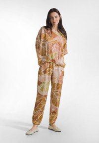 Dwuczęściowy strój wykonany z lekkiej tkaniny, z brązowym tłem i dużymi, kolorowymi wzorami liści w odcieniach różu i zieleni. Luźny krój.