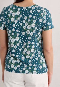 Krátký rukáv, zelené květinové tričko s bílými květy a tečkovanými vzory, oblé výstřih a měkká bavlněná textura.