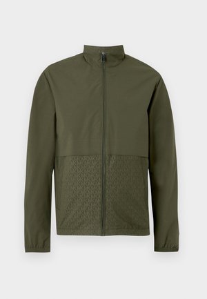Olivengrønn jakke med hel glidelås, høy krage, lange ermer, elastiske mansjetter og diskret "MK" monogrammønster på nedre frontpaneler.