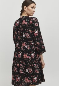 Abito nero a fiori con fiori rosa e bianchi a cinque petali. Presenta maniche lunghe, vita arricciata e gonna svasata. Tessuto leggero.