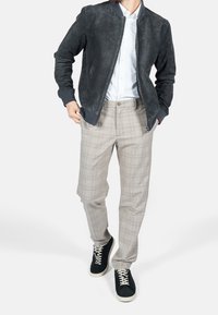 Graue Wildleder-Bomberjacke, weißes Hemd, helle karierte Hose und schwarze Sneaker mit weißen Sohlen. Strukturiertes Gewebe und moderne Passform.