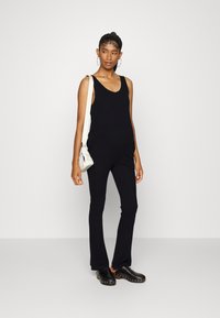 Macacão preto canelado com decote redondo, pernas largas e alças finas. Combinado com tamancos pretos e uma pequena bolsa branca.