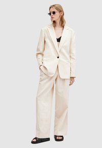 Completo beige chiaro a righe sottili realizzato in tessuto testurizzato, dotato di blazer con un solo bottone, pantaloni a gamba larga e sandali neri senza tacco.
