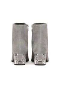 Botas de tobillo de ante gris con cierre de cremallera y un llamativo tacón decorativo metálico que presenta patrones geométricos. Textura suave en general.