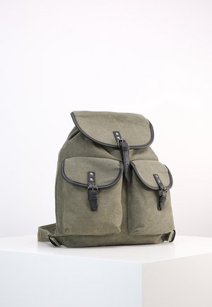 Olijfgroene canvas rugzak met zwarte lederen gespen, voorzien van één hoofdflap en twee voorzakken, geplaatst op een wit oppervlak.