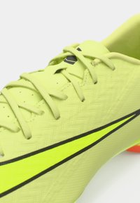 Fényes sárga-zöld sportcipő fűzőkkel, texturált felsőrésszel és merész neon sárga-fekete csíkkal. 