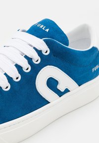 Modré semišové tenisky s bílými tkaničkami, bílým detailem "F" na boku a bílou podrážkou, s nápisem "FURLA" na jazyku a boku.