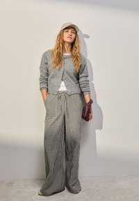 Grå cardigan, hvid skjorte og sort-hvide ternede bukser med brede ben. Holder en tekstureret lilla pung. Afslappet påklædning egnet til forskellige situationer.