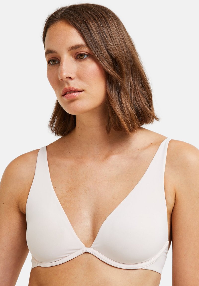 Soutien-gorge léger, doux, rose pâle avec un décolleté en V profond, larges bretelles et texture lisse. Aucun accessoire visible ni motif.