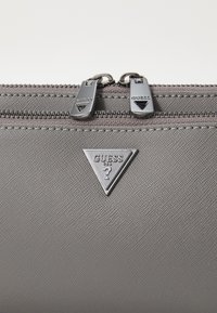 Portafoglio in tessuto grigio con texture, dotato di un logo triangolare argento e doppie cerniere argento con tiranti brandizzati.