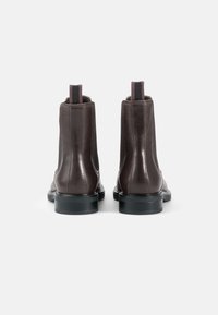 Brown leather chelsea boots featuring a smooth finish, elastic side panels, and contrasting pull tabs. Black rubber soles complete the design.