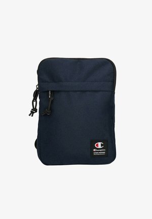 Kleine dunkelblaue Stoff-Schultertasche mit Frontreißverschlusstasche und Champion Markenlogo-Patch nahe der unteren rechten Ecke.