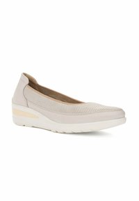 Zapato de color beige claro, tipo slip-on, con una parte superior texturizada, un tacón bajo tipo cuña y una suela blanca de contraste. Presenta un acabado exterior suave.