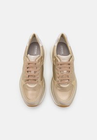 Světlé béžové tenisky s hladkým syntetickým koženým svrškem, kulatou špičkou, béžovými tkaničkami a gumovou podrážkou. Stříbrné detaily poblíž paty.