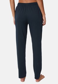 Adult wearing dark navy elastic waist relaxed-fit pants, shown from the back, barefoot against a plain light background.