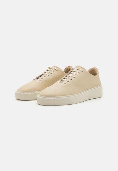 Beige lærersneakers med avrundet tå, snøring og teksturert hvit gummisåle. Minimalistisk stil uten fremtredende mønstre.